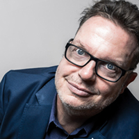 Headshot of a middle-aged white man with glasses against a tan background.